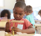 African American boy working with wooden shapes while sitting at a desk