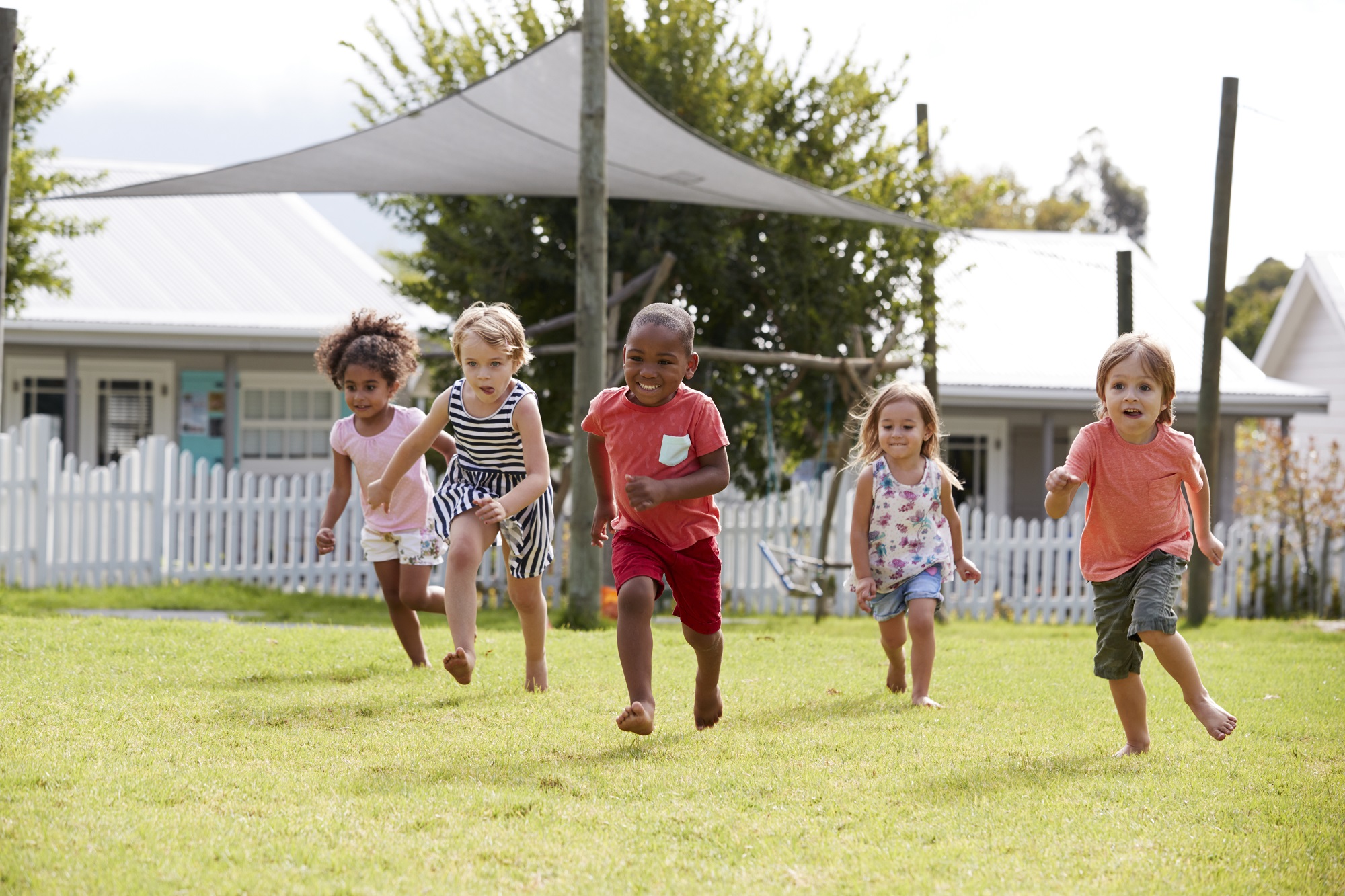 A group of preschool-aged kids running in a backyard