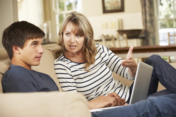 A mother and teenage son sit on a couch looking at a laptop together.