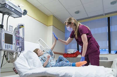 A boy in a hospital bed high-fives a nurse.
