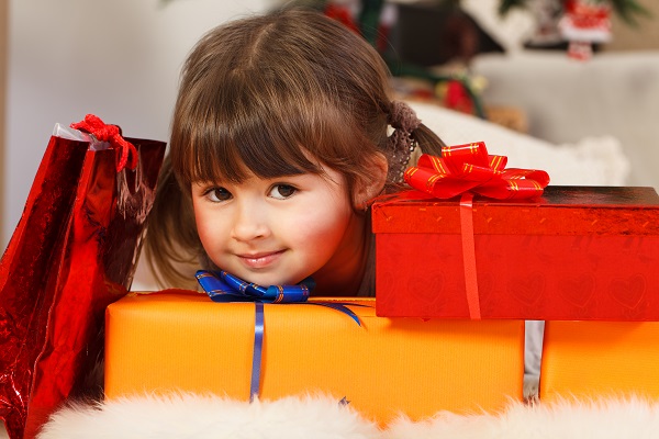 A young girl peeks her head around a stack of wrapped presents.