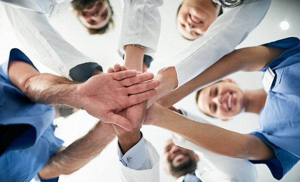 A group of doctors put their hands in a pile while standing in a circle, as seen from below.