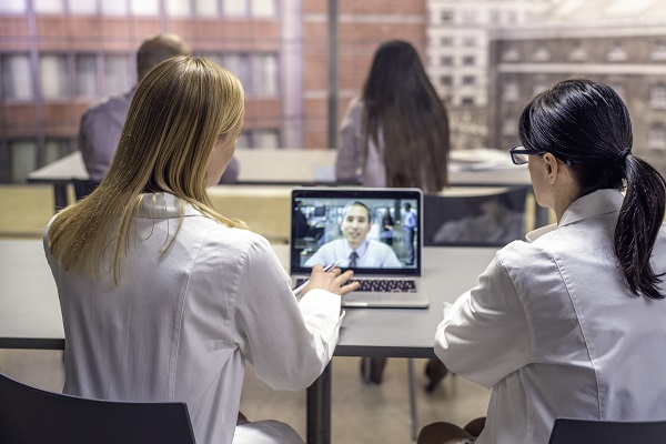 Two female health care providers watch a web conference on a laptop.