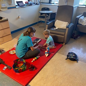 A music therapist sits on a red mat with a child for a music session at Children's National Hospital.
