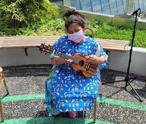 A young girl plays a ukulele while sitting in the Healing Garden.
