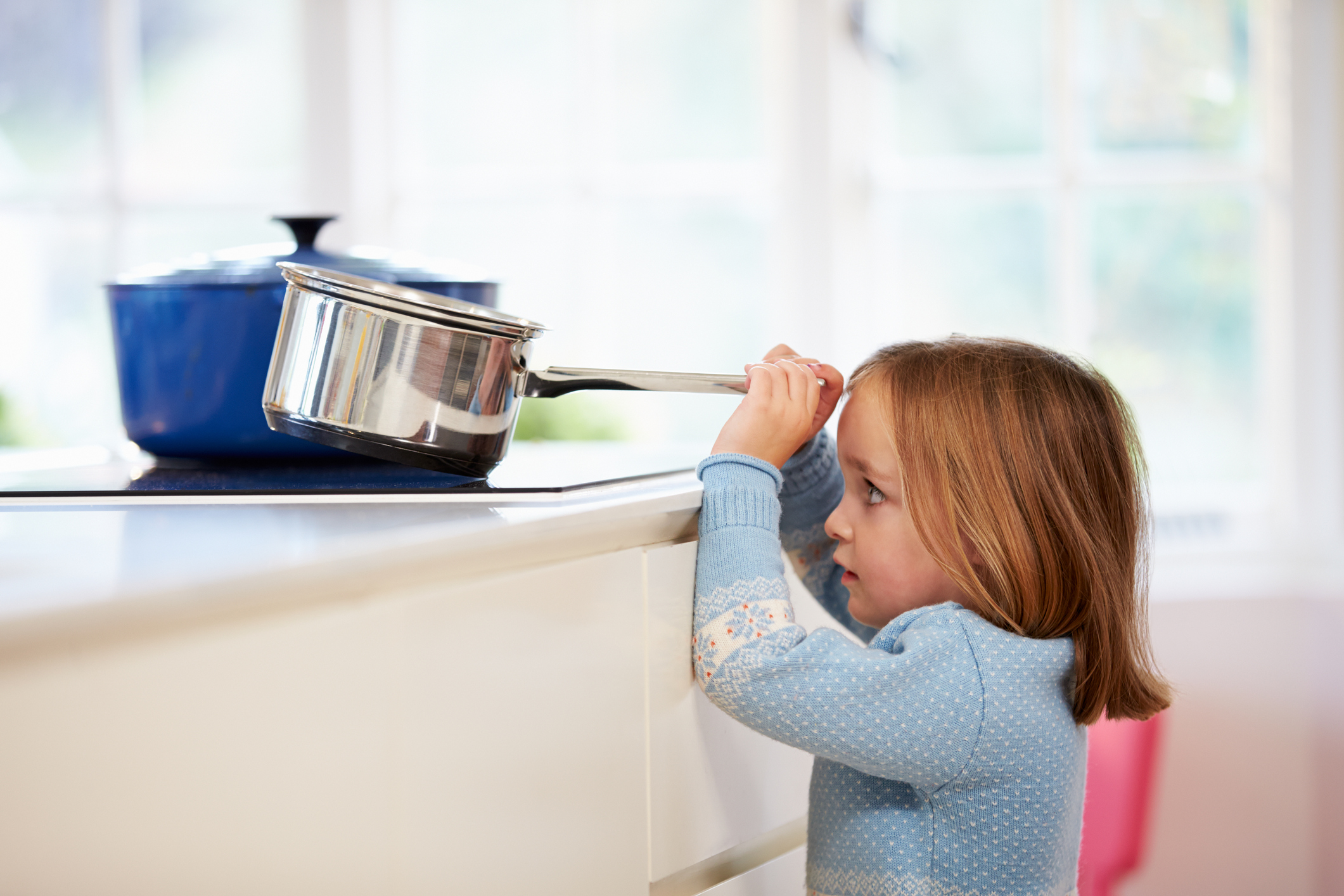 Little girl pulling pot off of stove