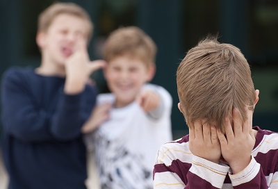 A boy covers his face with his hands as other boys bully him nearby.