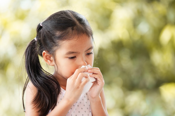 A young girl wipes her nose with a tissue.