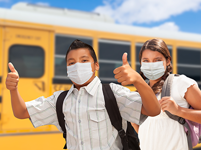 masked kids giving thumbs up in front of school bus