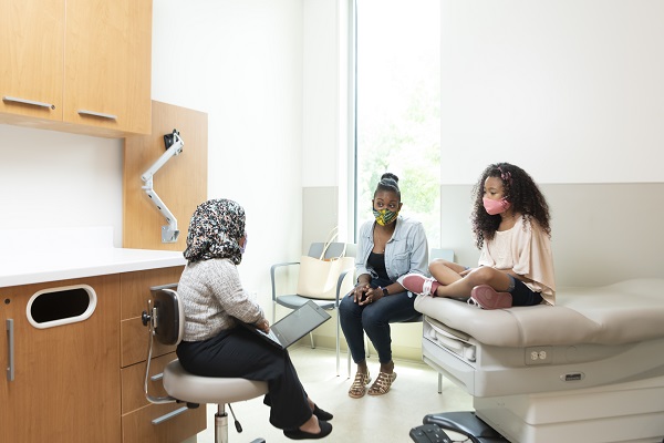 A healthcare provider talks to a teen girl and her mom in an exam room.