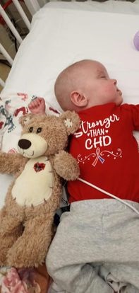 Claire sleeping in a hospital bed wearing a red "Stronger than CHD" onesie.