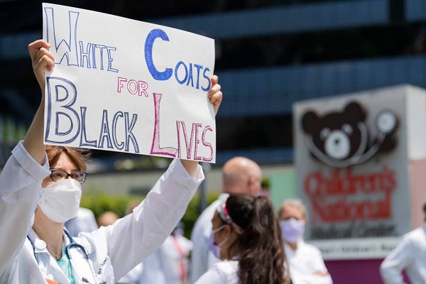 A health care provider holds up a sign that reads "White Coats for Black Lives" during a demonstration at Children's National Hospital.